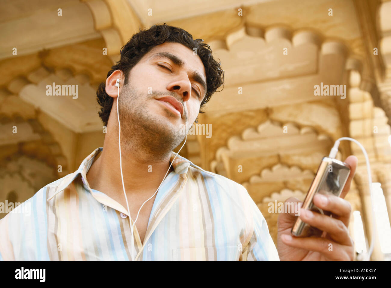 Ángulo de visión baja de un joven escuchando música en auriculares con los ojos cerrados, el Fuerte de Agra, Agra, Uttar Pradesh, India Foto de stock