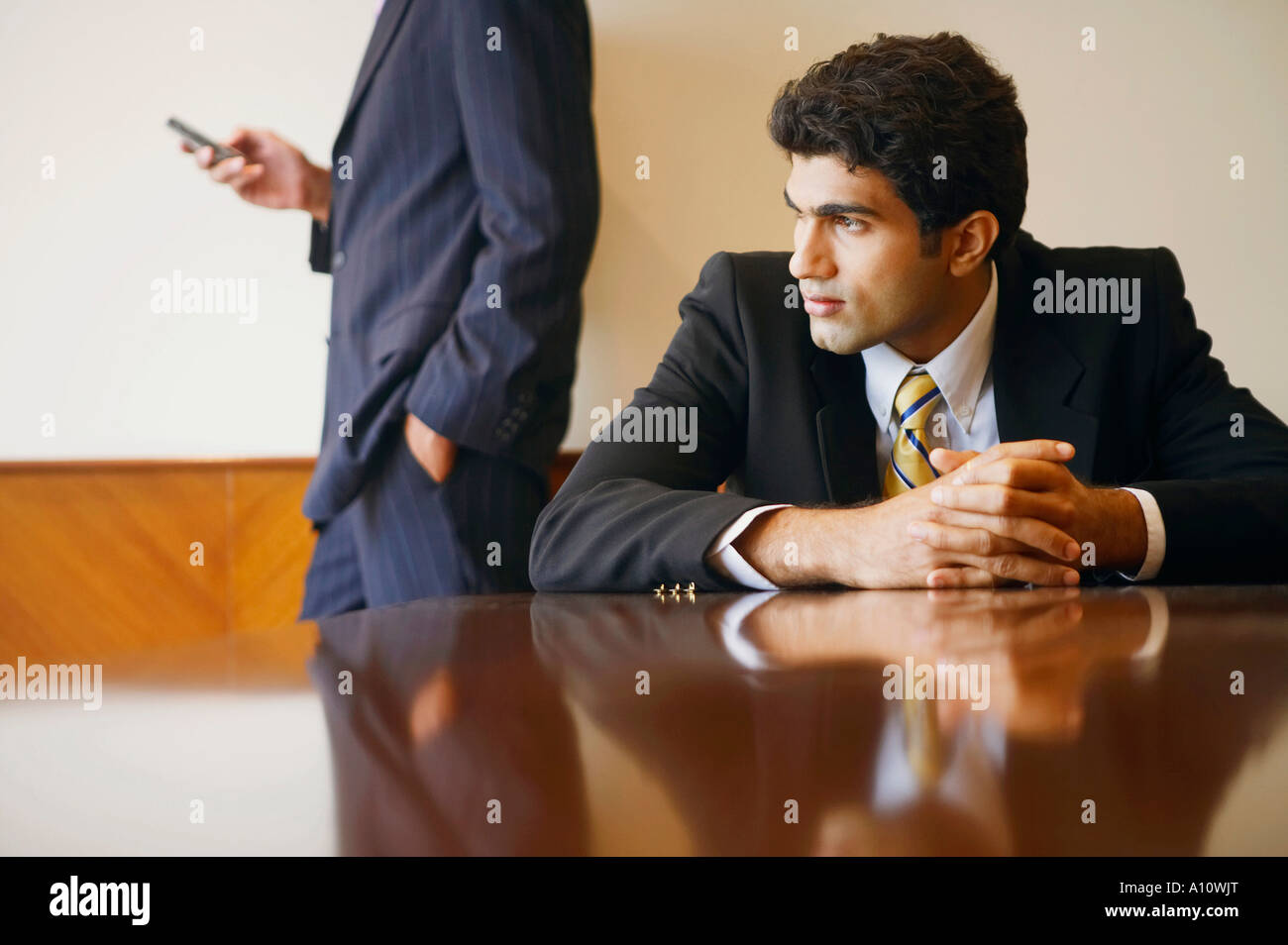 Close-up de un empresario sentado en una mesa con otro sujetando un teléfono móvil detrás de él Foto de stock