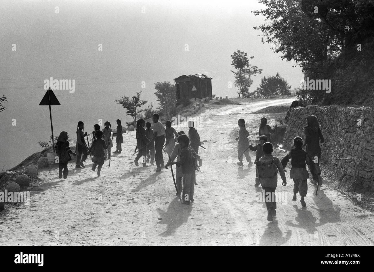 B/W de niños pequeños de un pueblo del Himalaya caminando por un camino de montaña a la escuela a primera hora de la mañana. Uttarkashi, Garwhal Himal, N. India Foto de stock