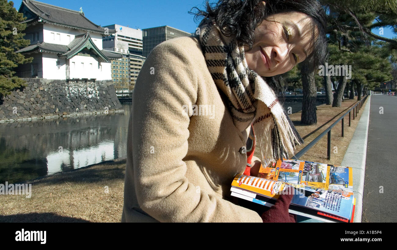 Mujer japonesa en abrigo y bufanda sentada y mirando a la cámara mientras  se lee una guía de los jardines del Palacio Imperial de Tokio JAPÓN  Fotografía de stock - Alamy