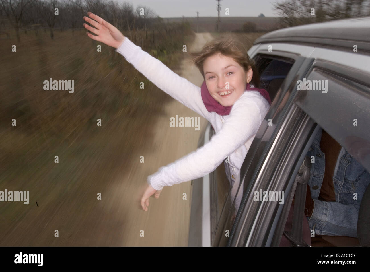Joven con un mantón color lila inclinado hacia fuera y saludando alegremente desde un coche a alta velocidad Foto de stock