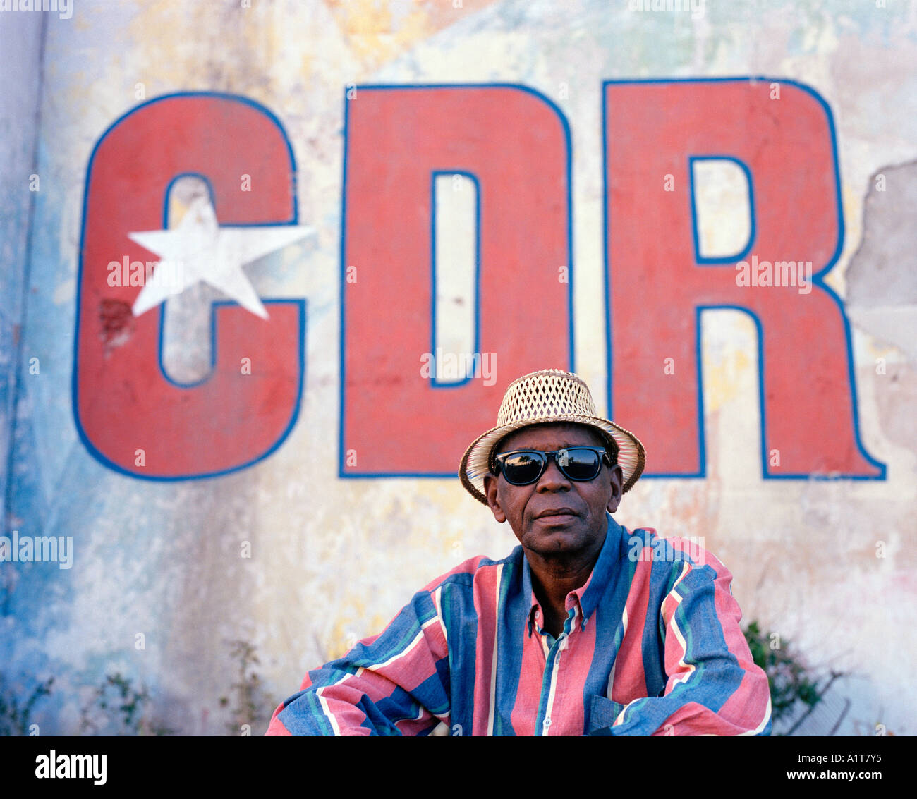 Hombre con gafas de sol sentado en frente de un CDR mural en La Habana, Cuba. Foto de stock