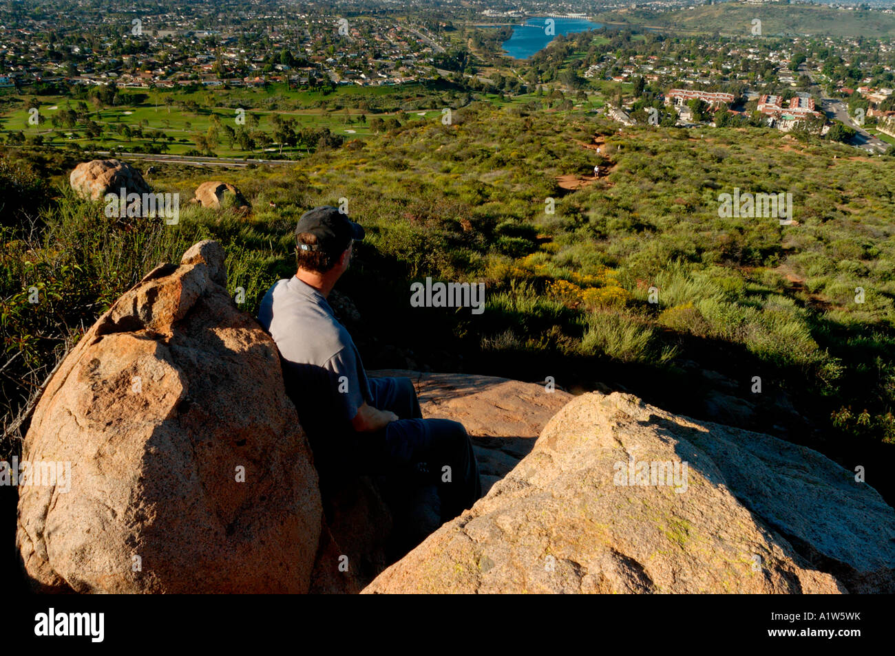 Hombre sentado sobre una roca a lo largo de senderos con vistas a San Diego. Foto de stock