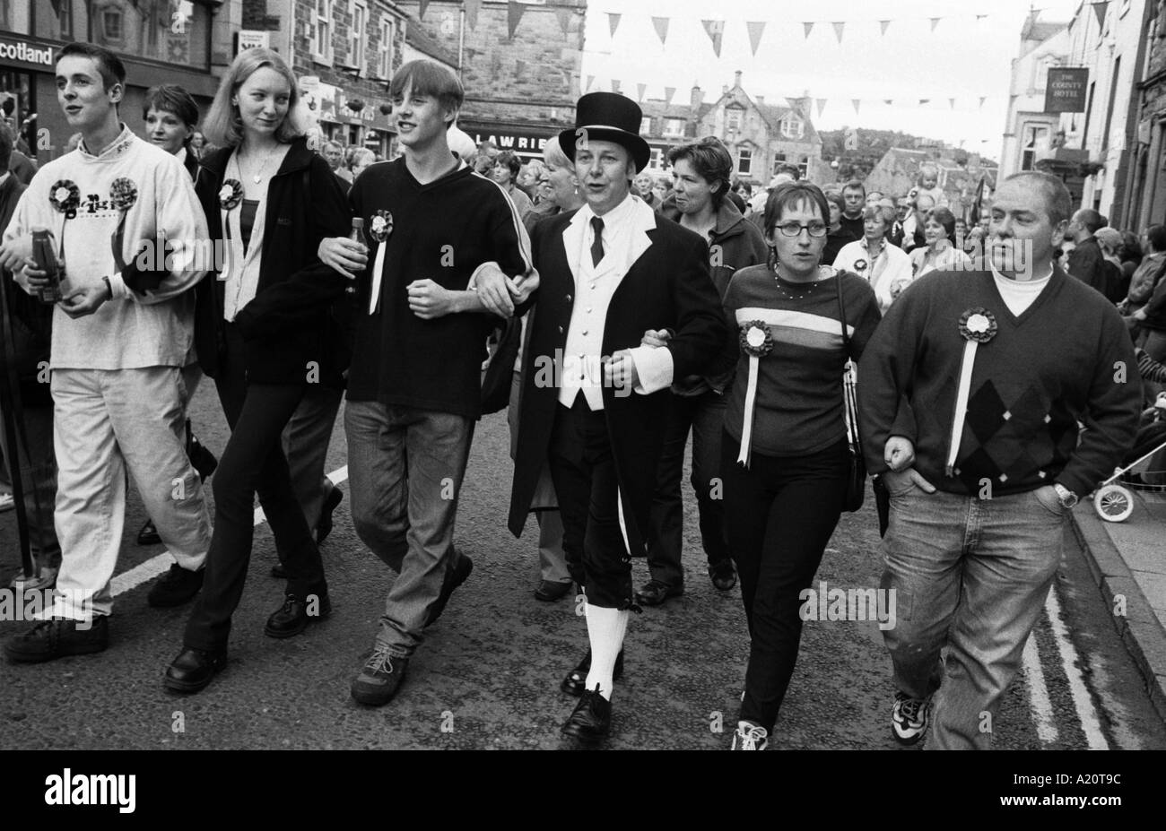 Personas cantando el granizo mañana sonriente mientras caminan por las calles de la ciudad durante las festividades de equitación común Selkirk, Escocia. Foto de stock