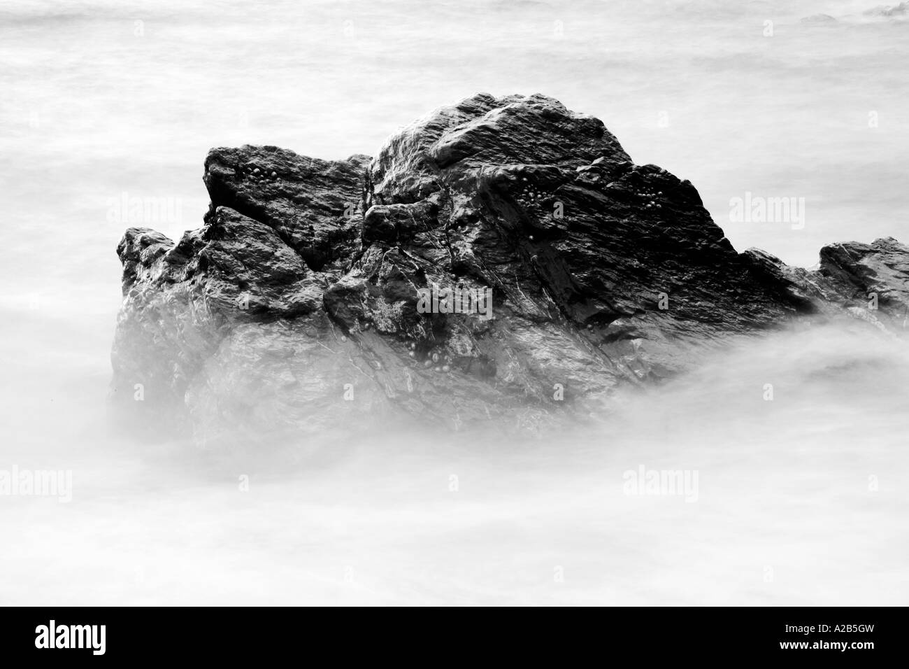 Monocromo en blanco y negro de una roca bañada por las olas de la costa del mar Foto de stock