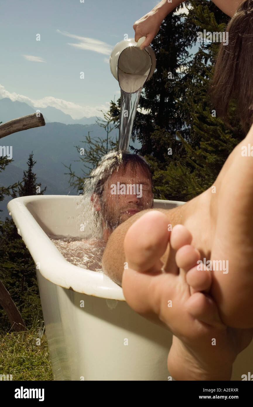 Joven tumbado en la bañera, joven mujer derramando agua sobre el hombre Foto de stock