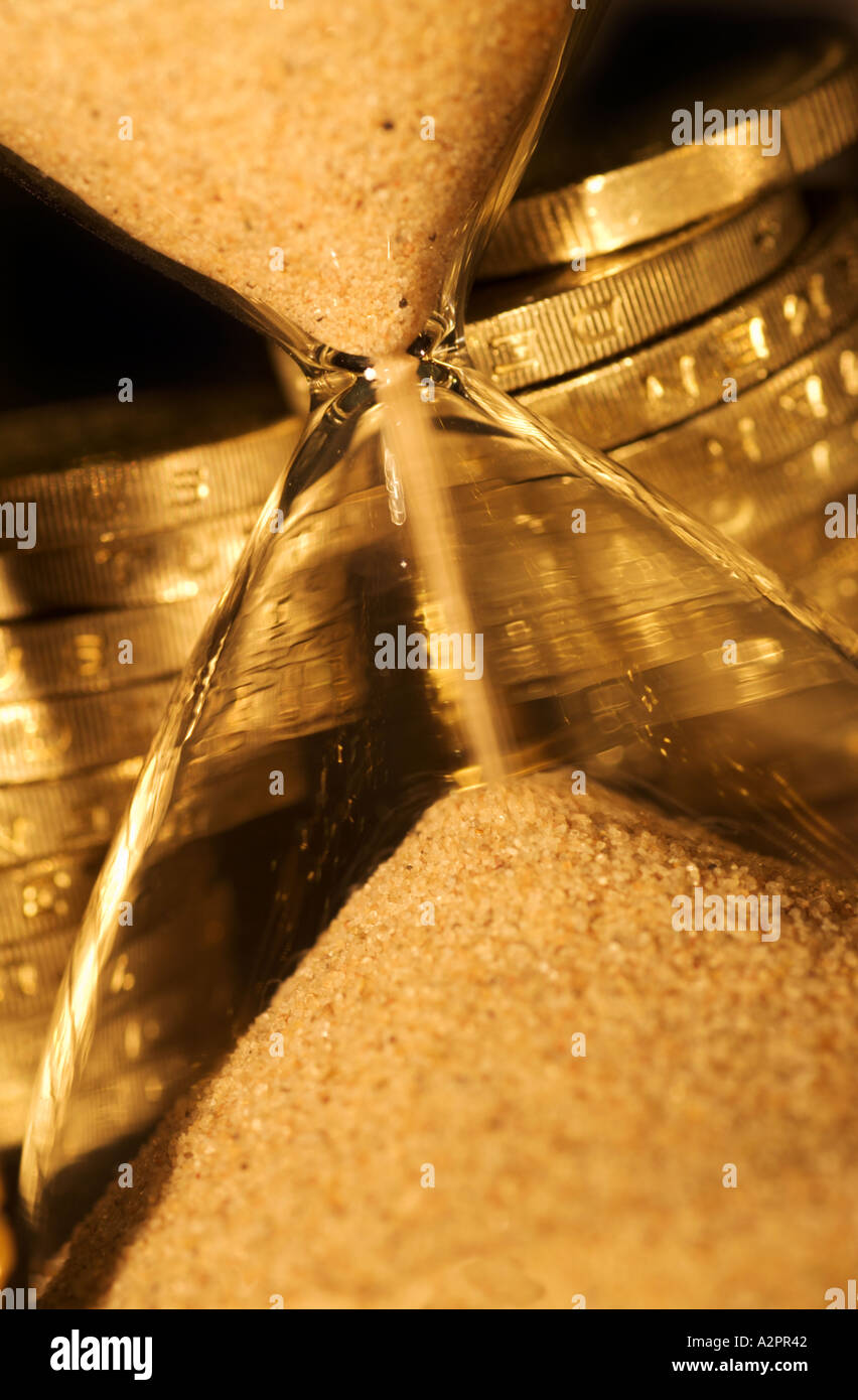 Tiempo y Dinero Arena corriendo a través de un cristal de hora y montones de monedas Foto de stock