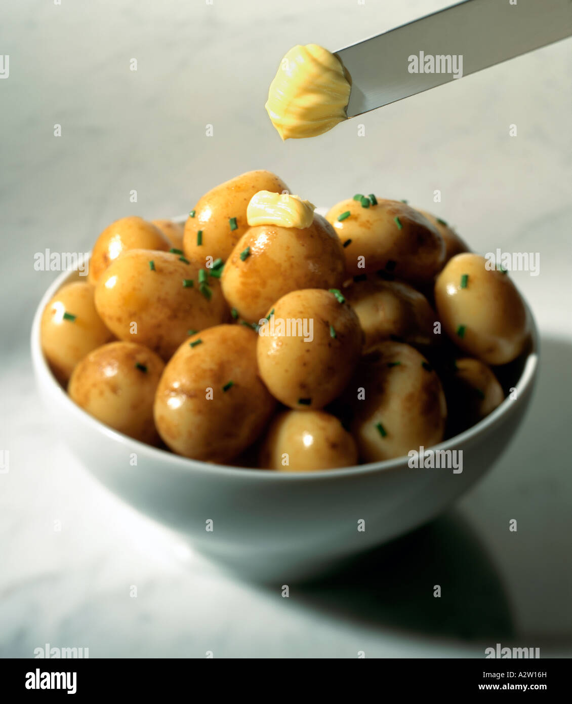 Nuevas patatas con cebollino picado y propagación en un recipiente blanco Foto de stock