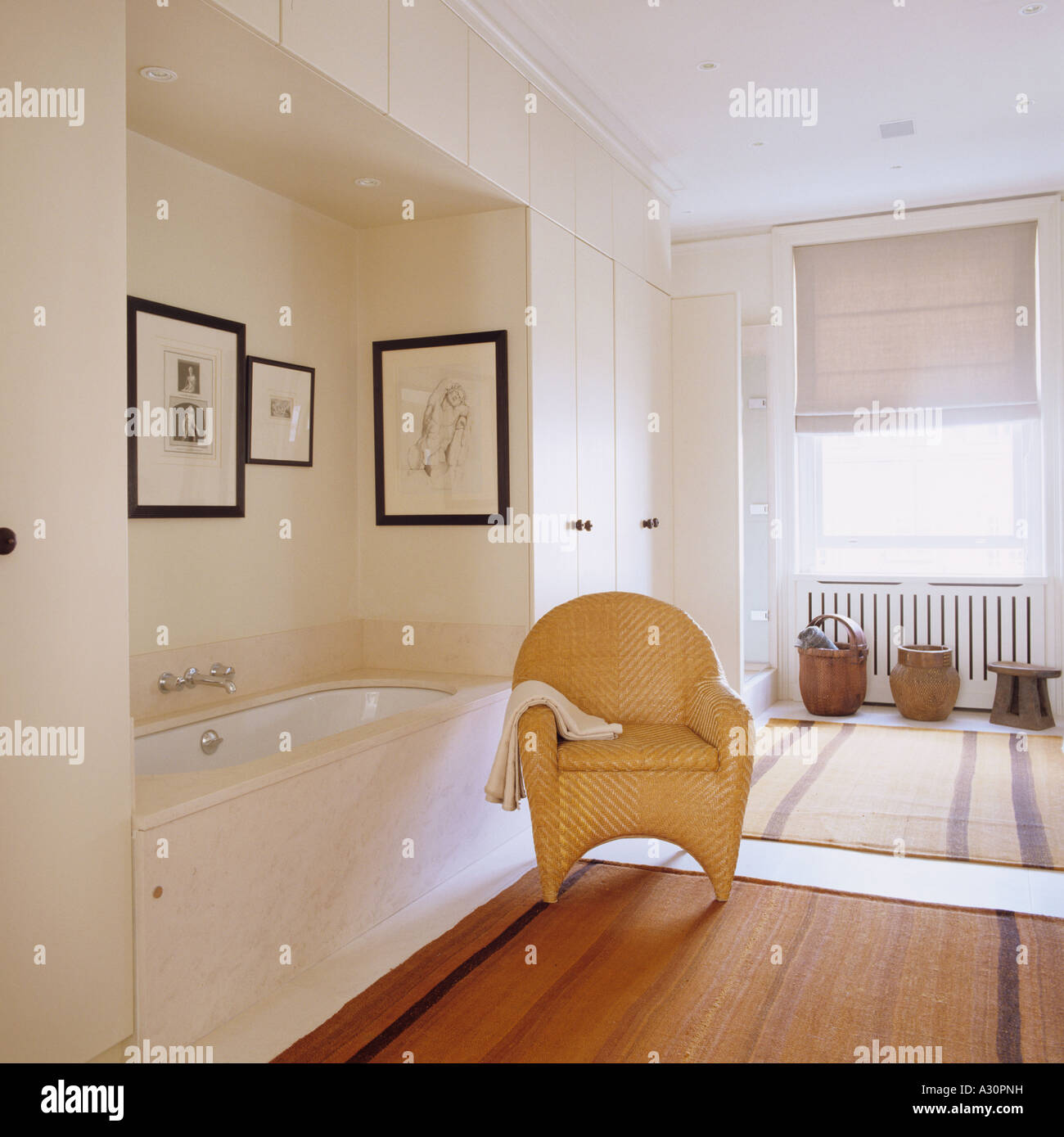 Silla de mimbre en el cuarto de baño con bañera empotrada y alfombras rayadas Foto de stock