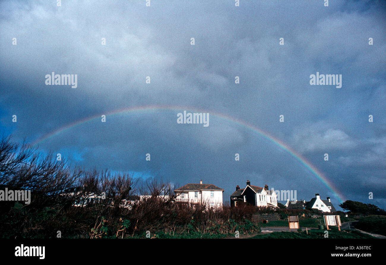 Amplio ángulo de visión de un arco iris en un cielo tormentoso con casas blancas Foto de stock