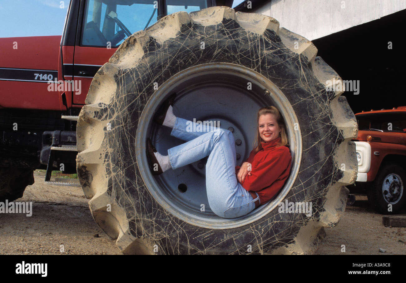 Una joven mujer vistiendo pantalones de mezclilla y una blusa roja sentada  dentro de la llanta de un neumático del tractor gigante en una granja en  Arkansas podría esto Fotografía de stock -