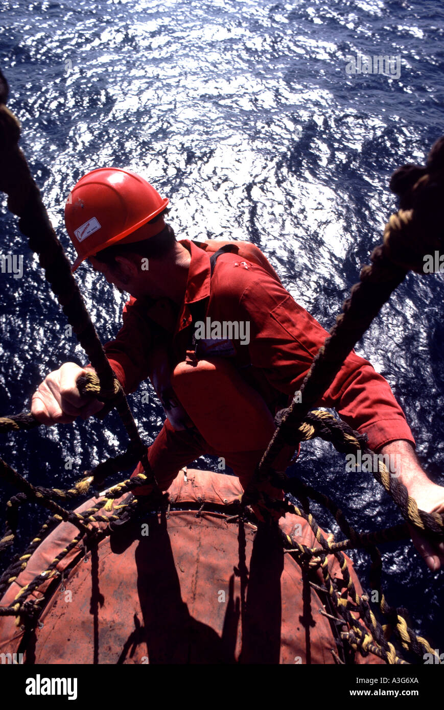 Valiente trabajador de la industria del petróleo y gas se ve abajo como él los saldos por encima de una plataforma off shore para realizar tareas de mantenimiento. Foto de stock
