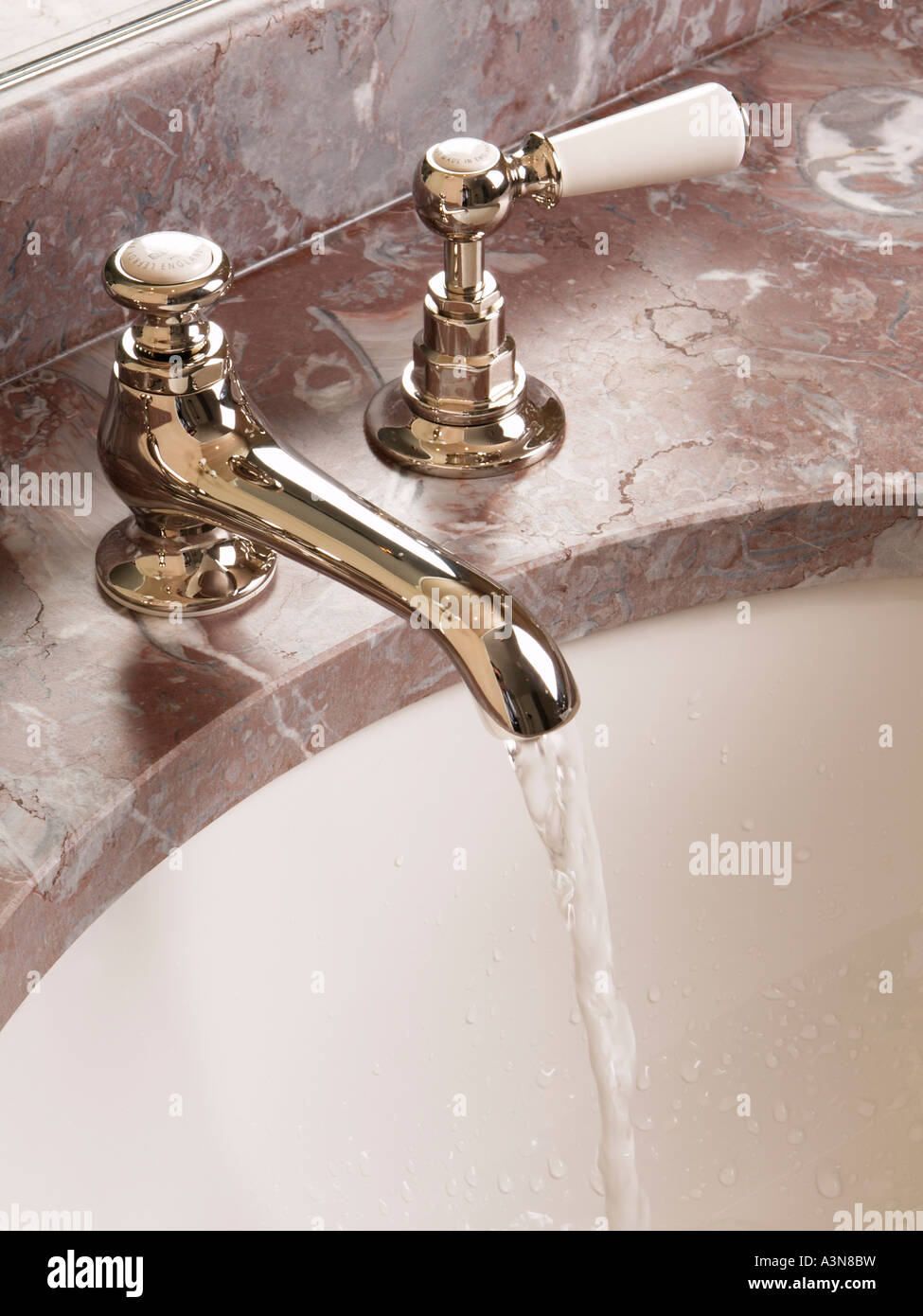 Grifo del baño antiguo clásico toca en la parte superior de mármol rosa del fregadero con agua corriente Foto de stock