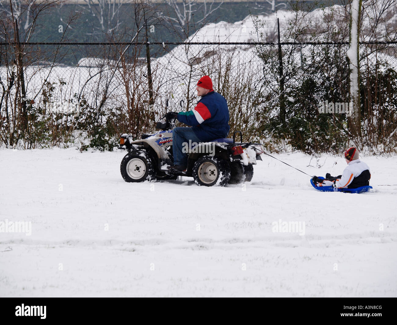 Padre montando en quad remolque tirando a su hijo a través de la nieve en un trineo trineo diversión invernal Breda Holanda Foto de stock