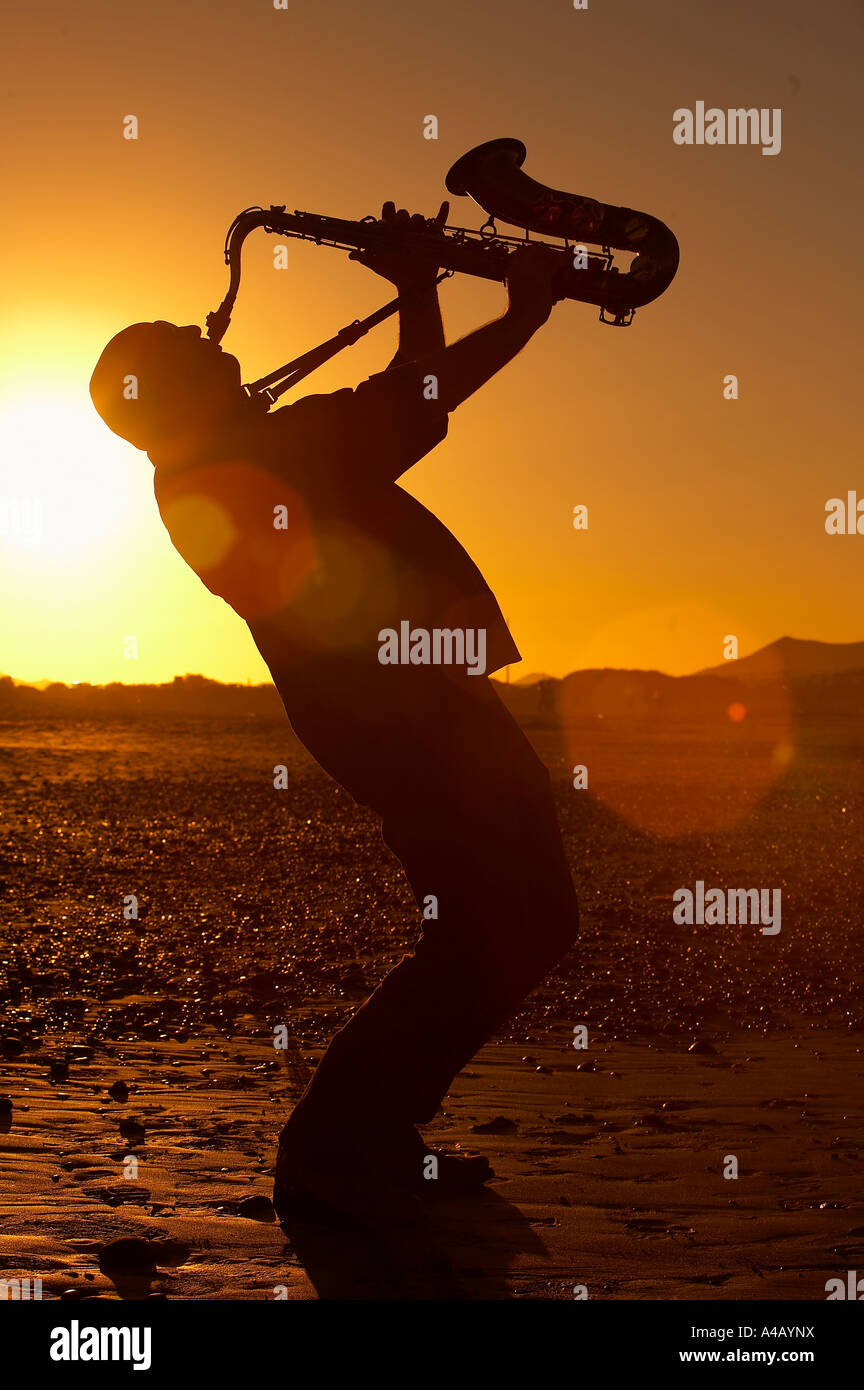 Silueta de hombre tocando el saxofón al atardecer Foto de stock