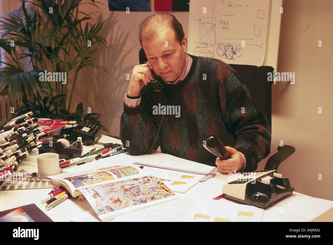 Director de arte con una agencia publicitaria o editorial en la recepción hablando por dos teléfonos. Foto de stock