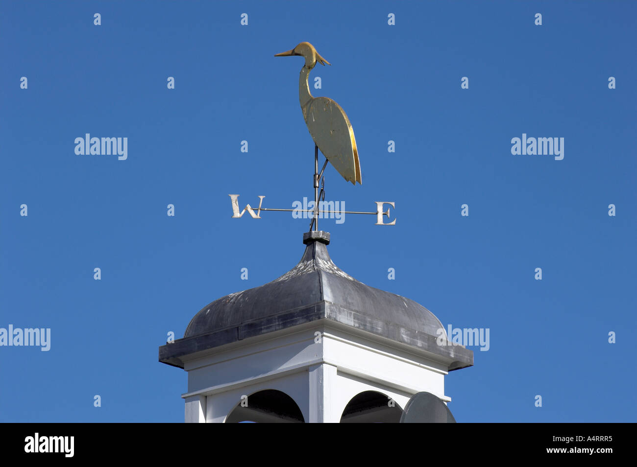 Veleta representando una cigüeña, adornando un tejado contra un cielo azul brillante. Foto de stock