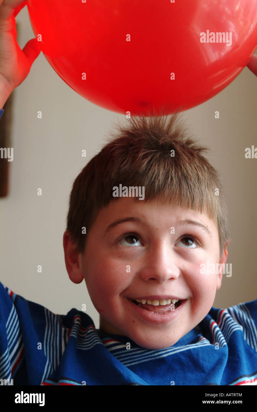 Un niño de 7 años tiene un globo rojo sobre su cabeza y la electricidad estática y tira de su pelo hacia el globo Foto de stock