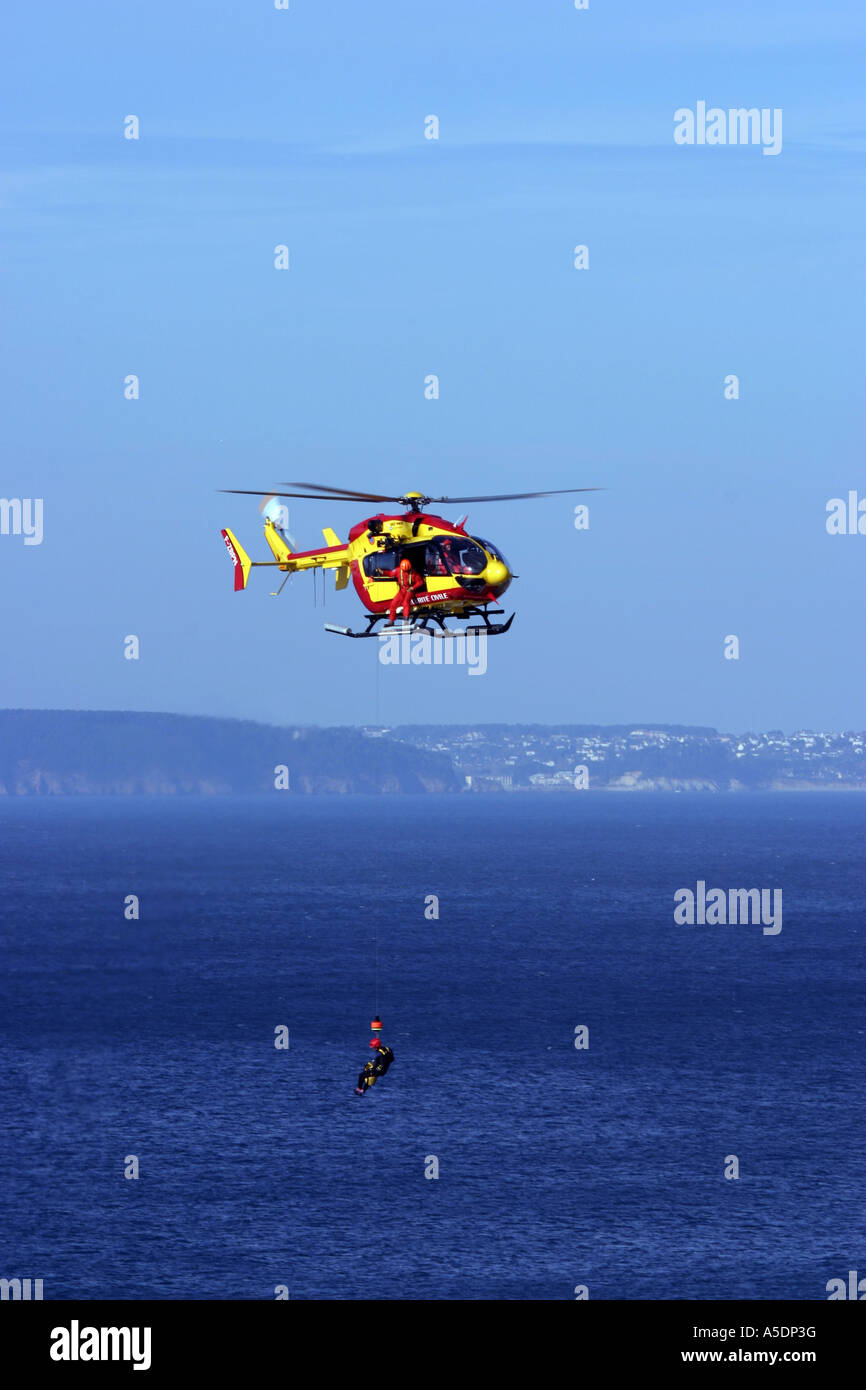 Un securite Civile helicóptero de rescate malacates de vuelo a bordo de un siniestro, Bretaña, Francia Foto de stock