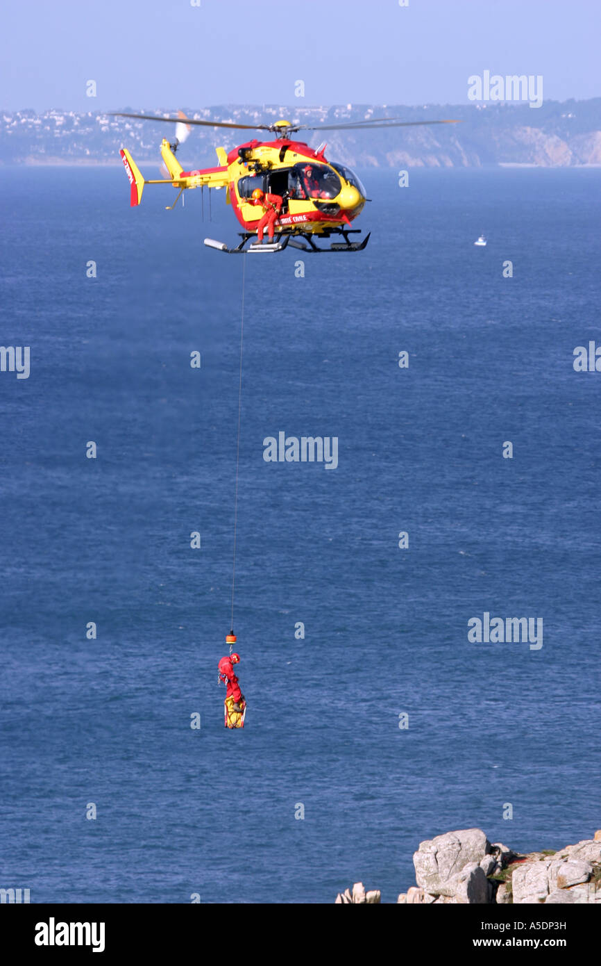 Un Securite Civile helicóptero de rescate malacates de vuelo a bordo de un siniestro, Bretaña, Francia Foto de stock
