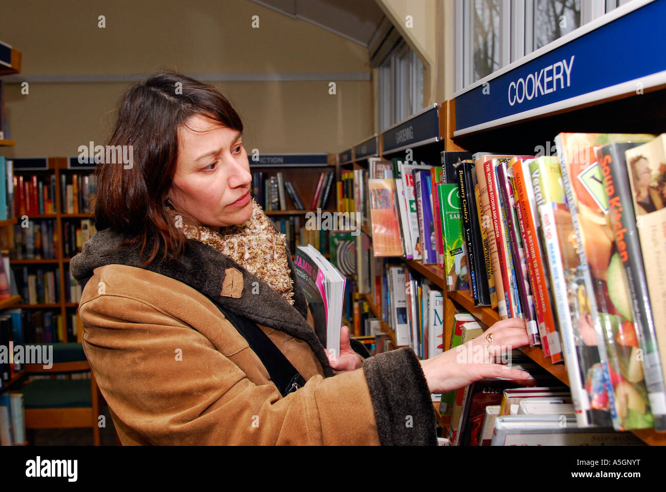 La mujer examina la sección libro de cocina en su biblioteca local, Kingston, Surrey, Reino Unido. Foto de stock
