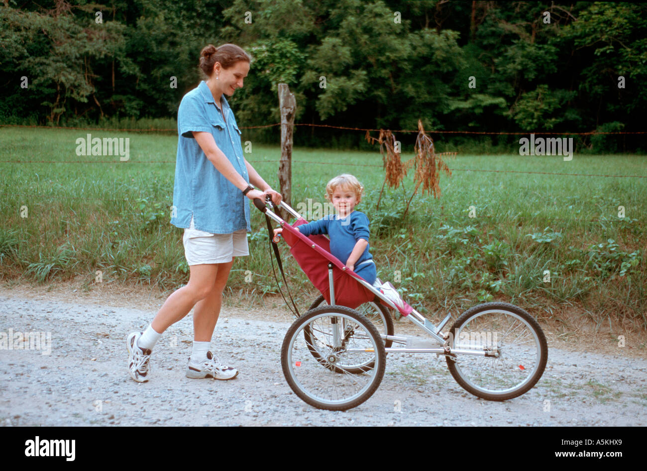 Una madre lleva a su niño un carril del país en un cochecito. Foto de stock