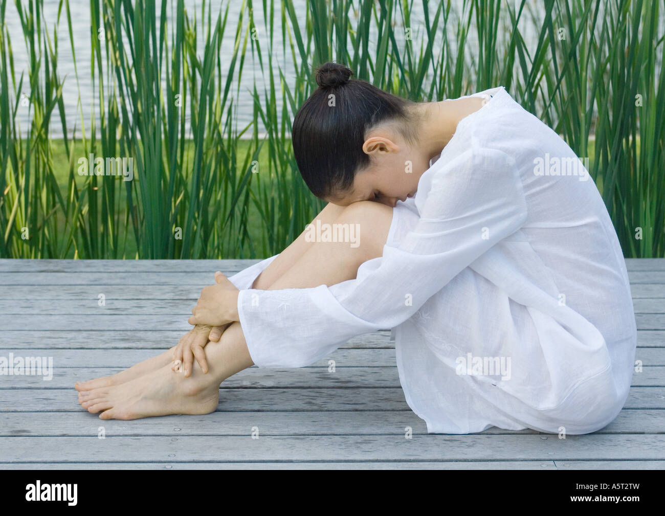 Mujer sentada en la cubierta con la cabeza en las rodillas Foto de stock