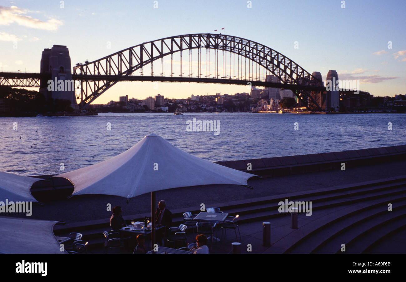 Sydney Harbour Bridge al atardecer con mesa y sombrilla en primer plano la gente cenando Foto de stock