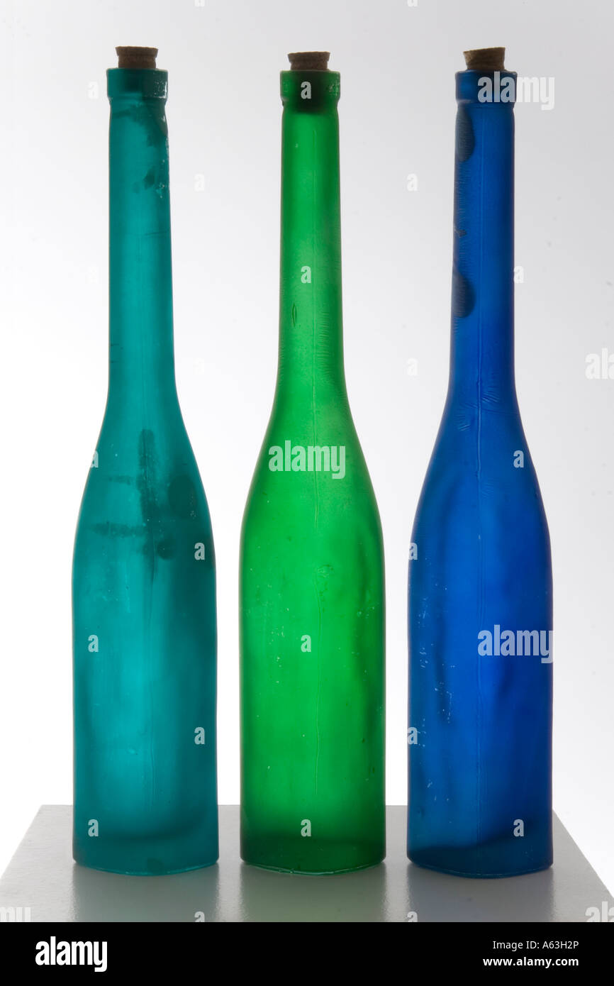 Sigue la vida de tres delgadas fabricadas a mano botellas con corchos retroiluminada para mostrar los colores azul turquesa y verde contra el blanco Foto de stock