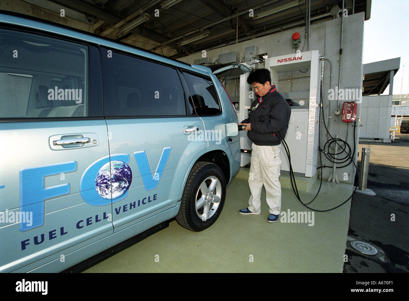 Un trabajador de Nissan Nissan recarga Fuel Cell Vehicle Coche eléctrico en una instalación de recarga en una planta Nissan en Japón Foto de stock