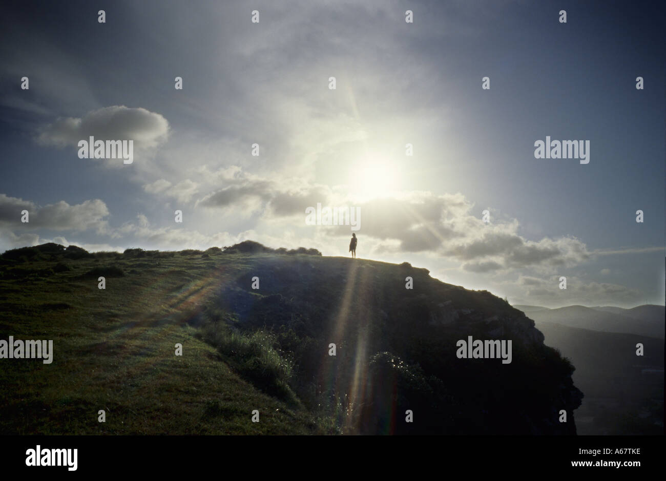 Solo la figura de pie en el acantilado de la costa montañosa peak silueteado contra el sol Foto de stock
