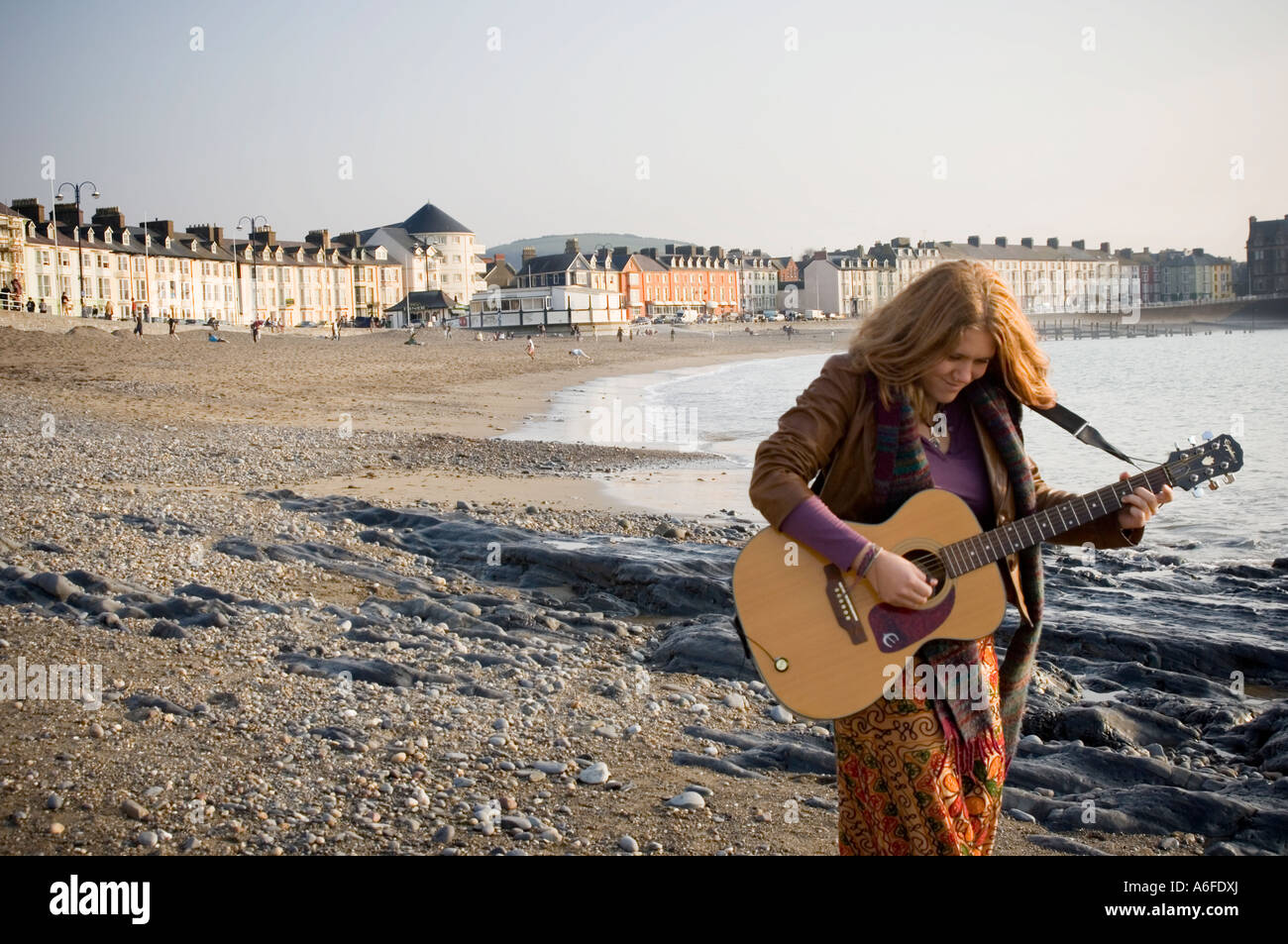 Joven Mujer hippie de pelo largo tocando la guitarra en la playa Gales Aberystwyth UK Foto de stock