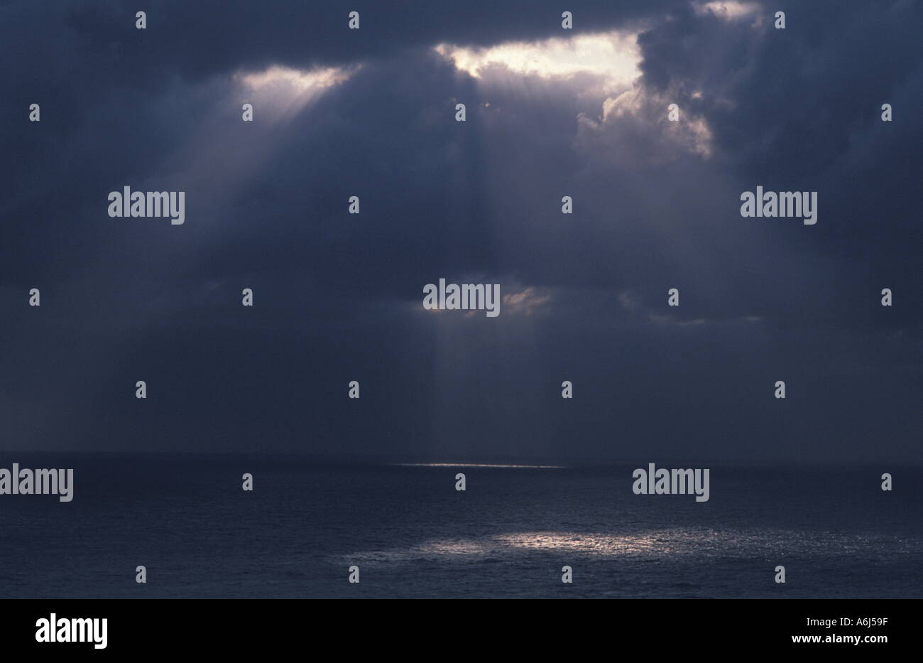 La luz brilla a través de nubes sobre el océano Foto de stock