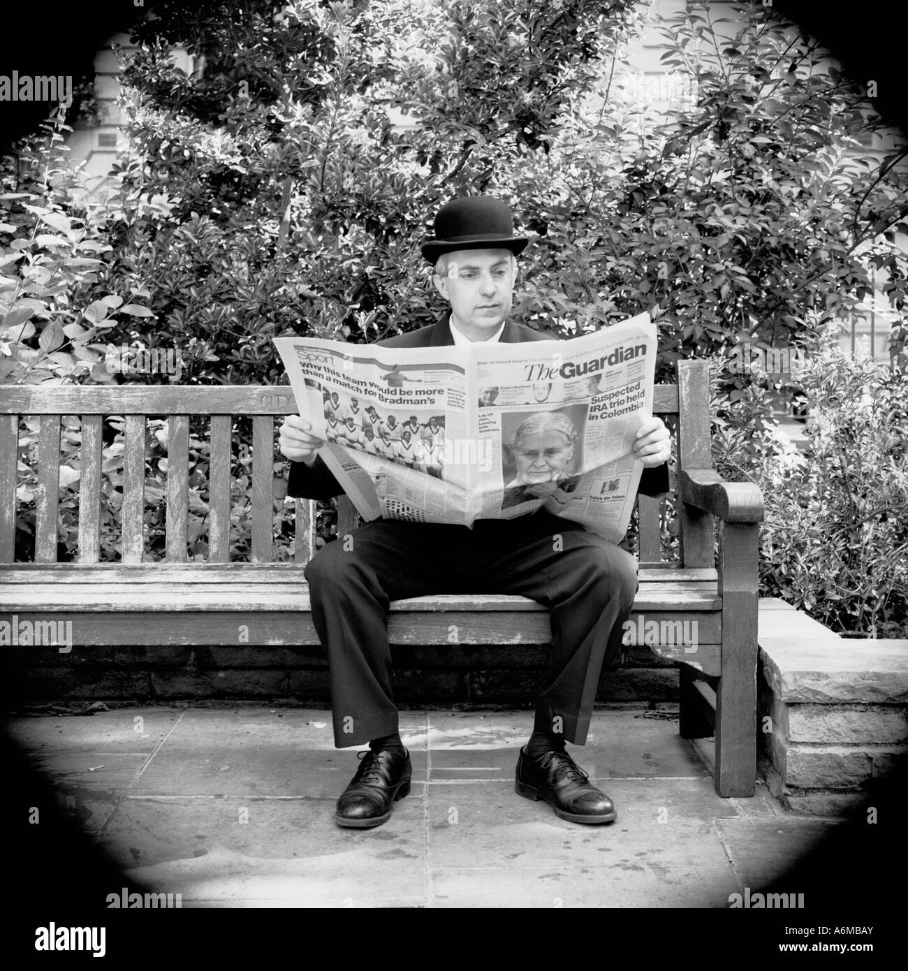 Hombre de negocios de la ciudad inglesa leyendo el periódico Guardian sentado en el banco en el parque de Londres Foto de stock