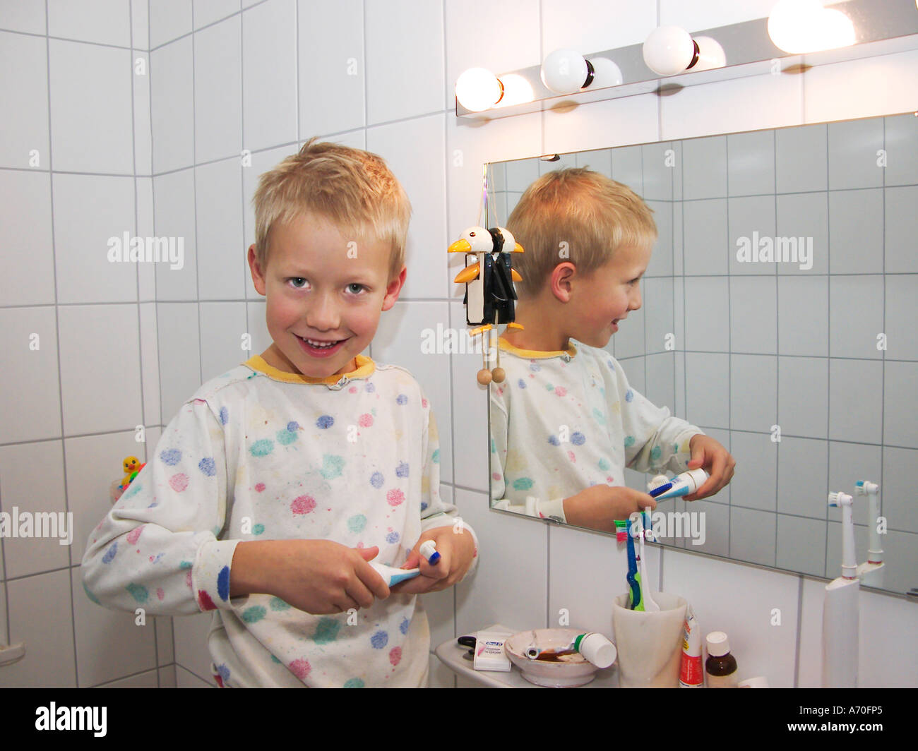 Pequeño de siete años de edad en pijama cepillando sus dientes reflejando en el espejo Foto de stock
