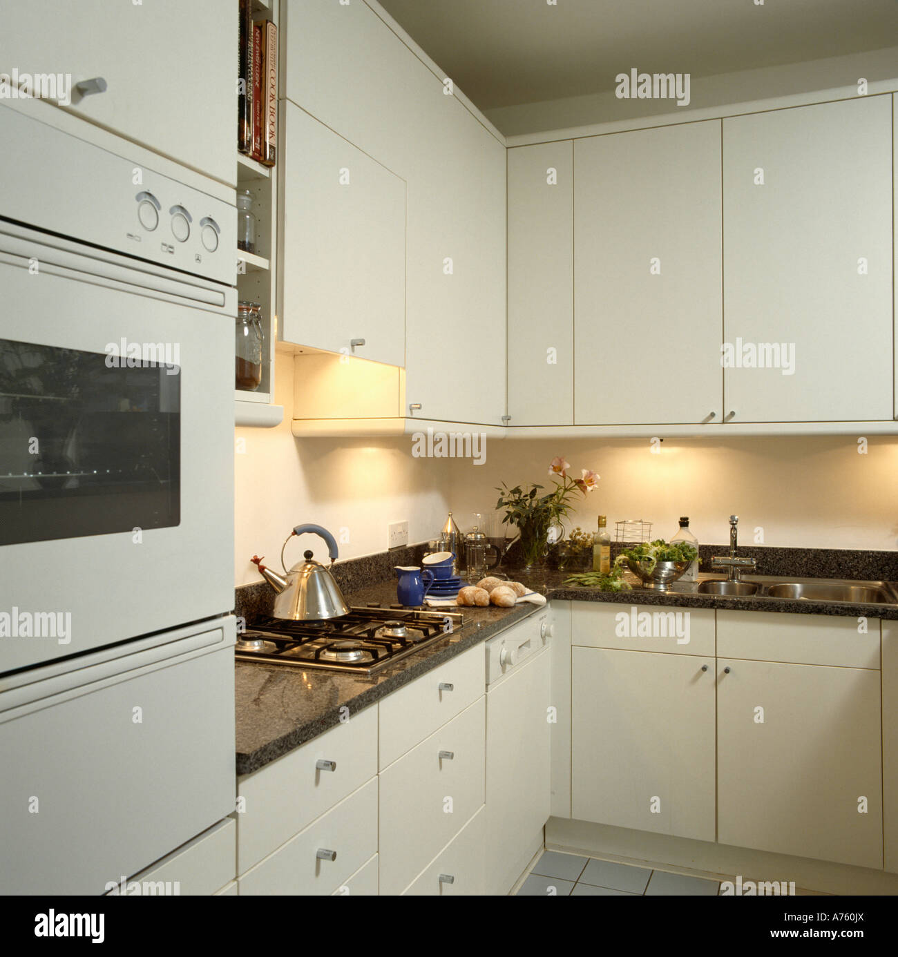 Blanca Pequeña cocina con horno montado en la pared y encimeras negro con  Alessi hervidor sobre encimera de gas Fotografía de stock - Alamy