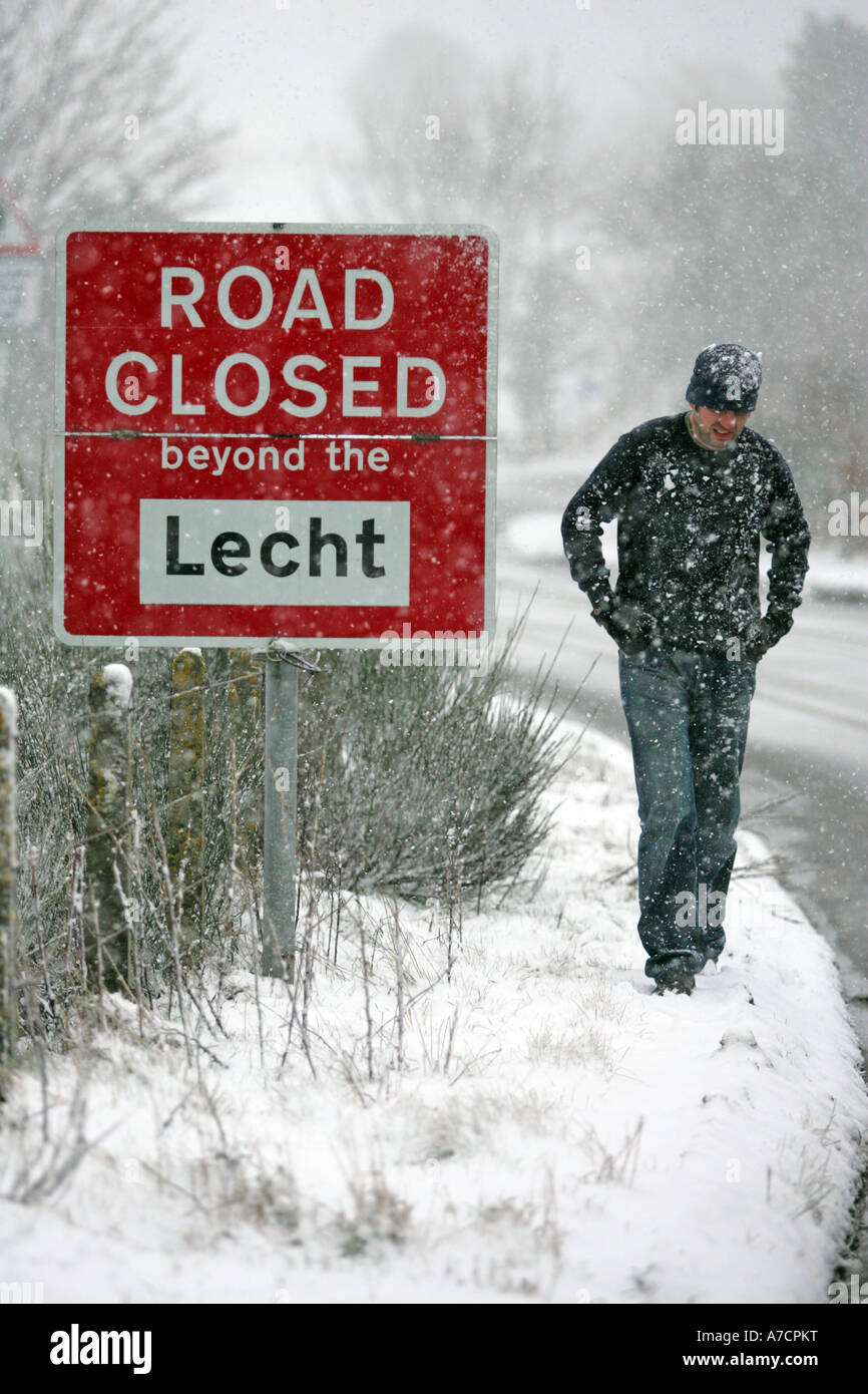 Hombre caminando a través de Blizzard durante tiempo de nieve en el invierno pasado el cartel de cerrado por carretera cerca del centro de esquí lecht Aberdeenshire Foto de stock