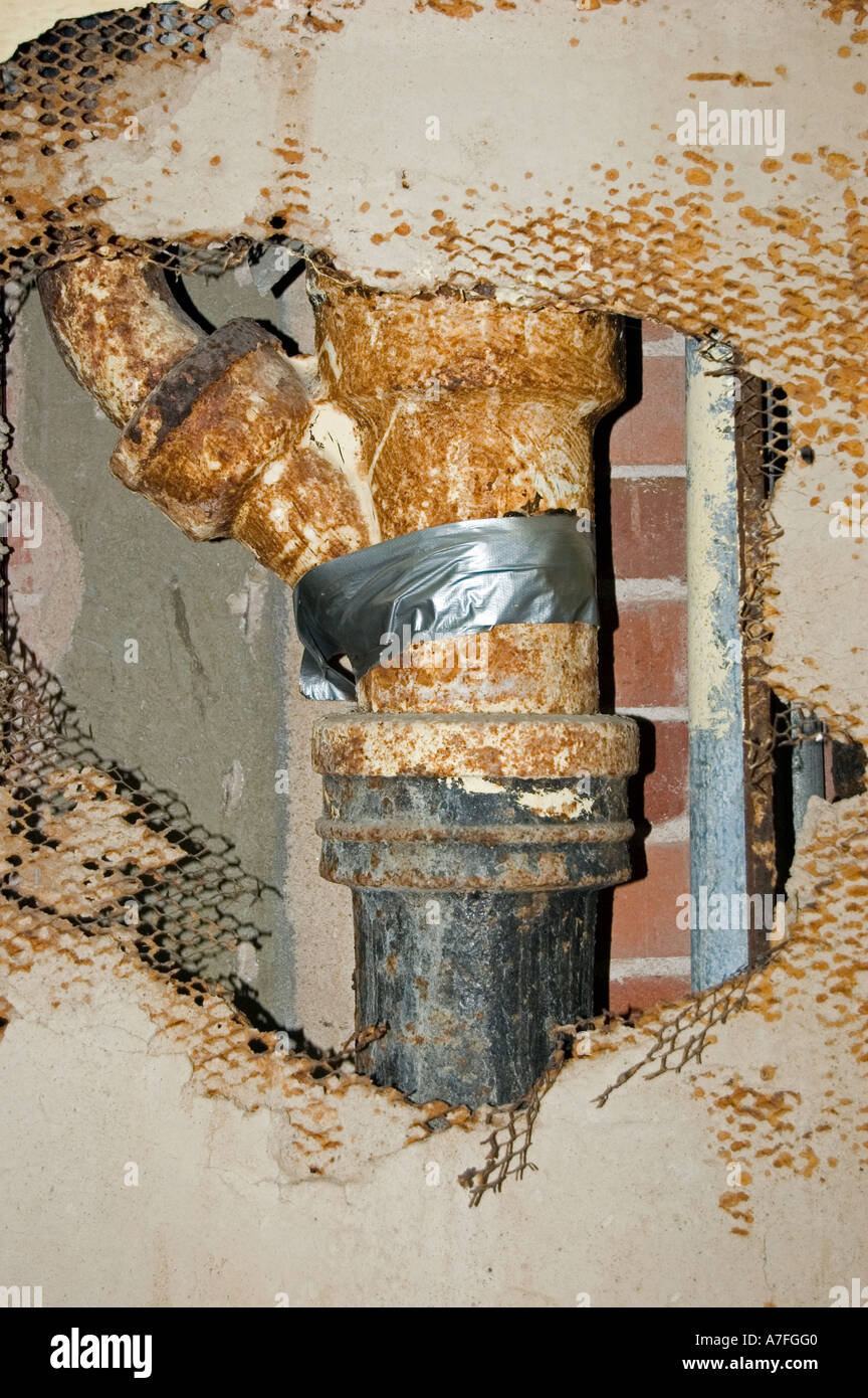 Tubo de hierro en el viejo edificio con el yeso grietas alrededor reparado con cinta adhesiva Foto de stock
