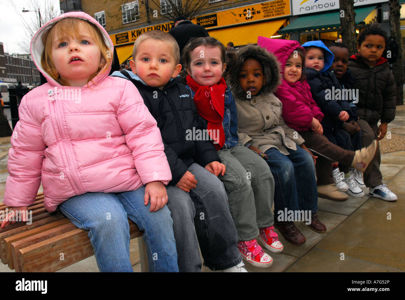 Grupo de 8 niños sentados en un banco, al oeste de Londres, Reino Unido. Foto de stock