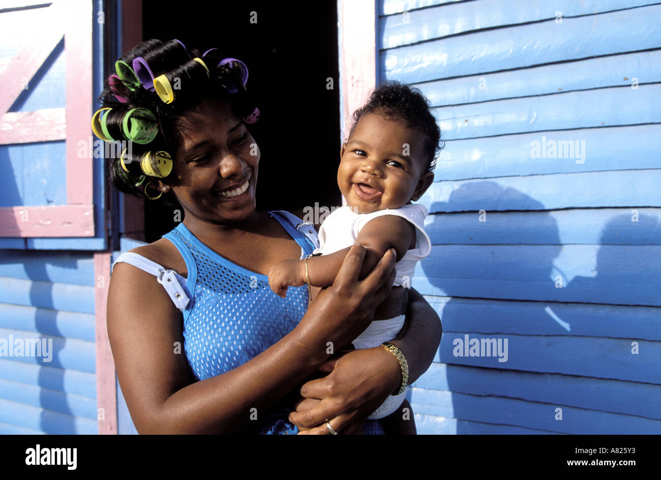Republica Dominicana Provincia De Samana Joven Mujer Sostiene A Su Bebe Frente A Una Casa De Color Fotografia De Stock Alamy