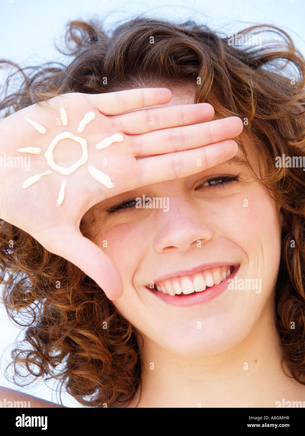 Adolescente sonriente con la figura de un sol dibujado en la crema solar en su mano piel clara deben estar protegidos contra los rayos UV Foto de stock