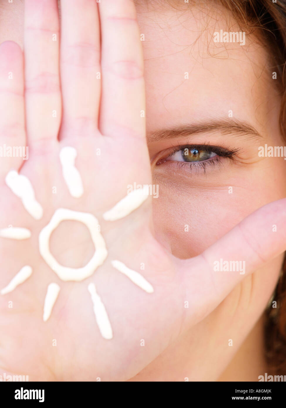 Las adolescentes los ojos y las manos closeup con la figura de un sol dibujado en la crema solar en su mano Foto de stock