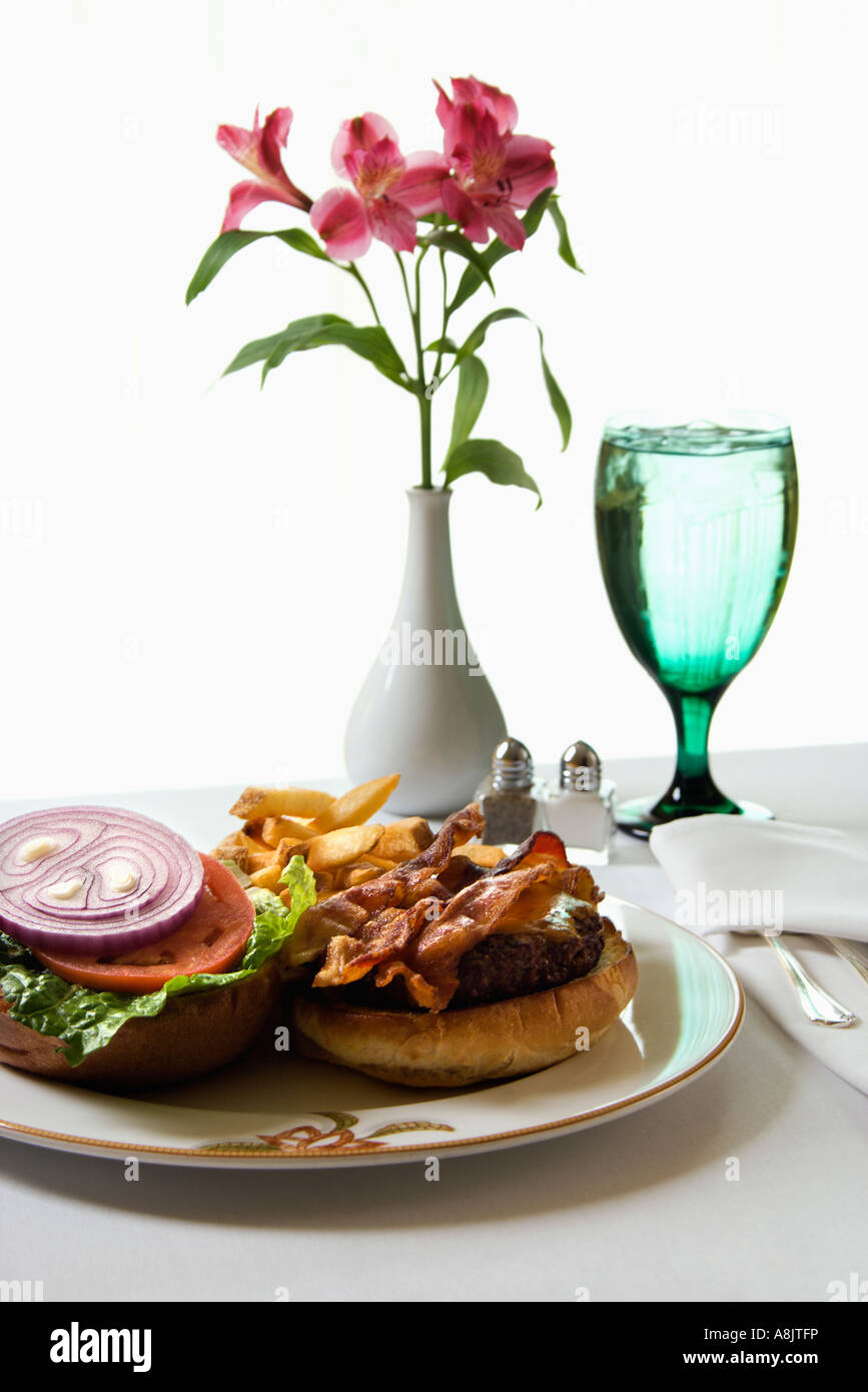 El Cheeseburger comida con flores y vaso de agua Foto de stock