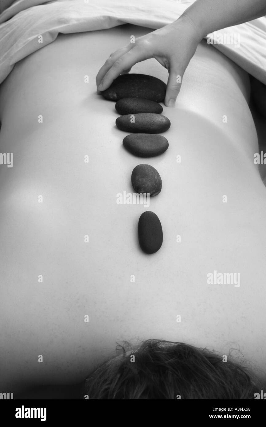 Lugares LMT piedras calentadas a lo largo de la columna vertebral del cliente masculino en un masaje con piedras calientes Foto de stock