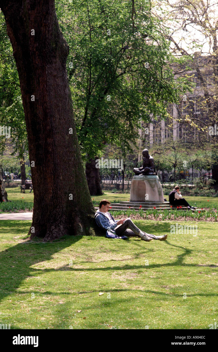 Hombre apoyado en un árbol en Tavistock Square en Londres el sol Foto de stock