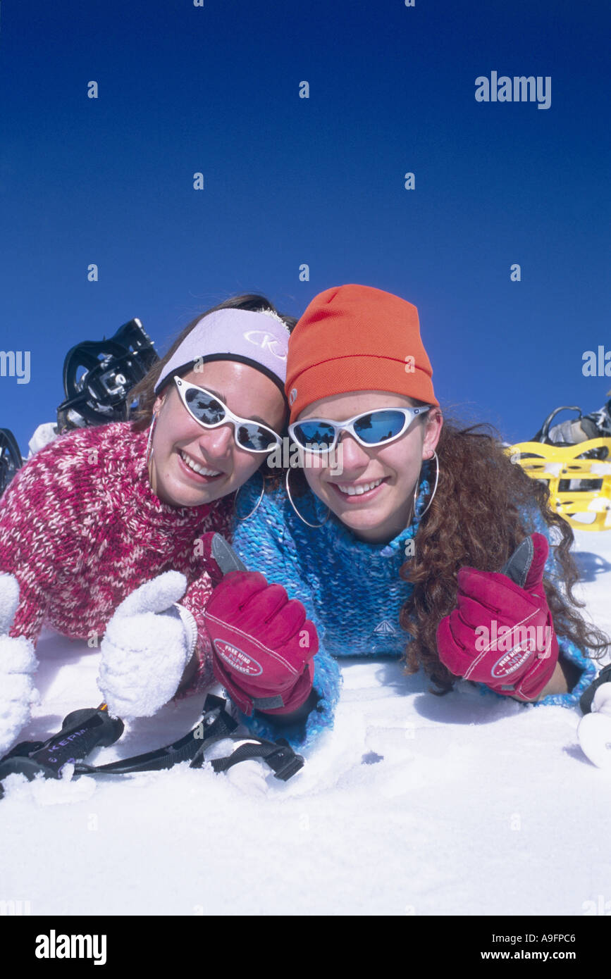 Dos niñas tumbado en la nieve, vistiendo gorras y gafas de sol. Foto de stock