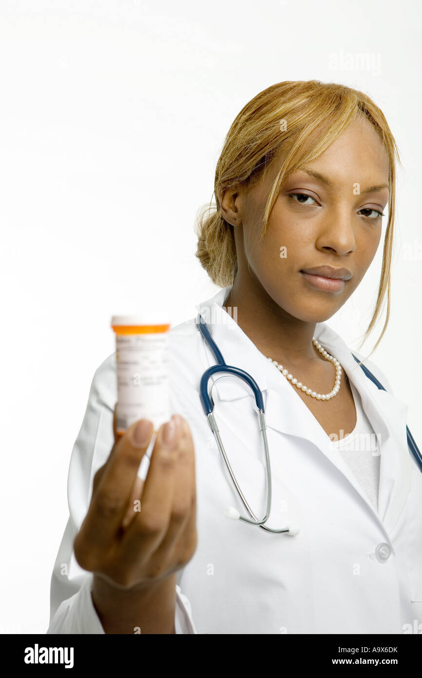 Joven doctora en una bata blanca y estetoscopio ofrece un frasco de medicamentos hacia el paciente Foto de stock