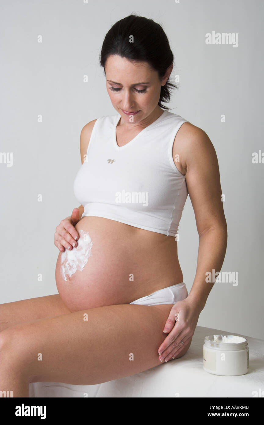 Mujer embarazada frota crema para el cuerpo en su estómago Foto de stock