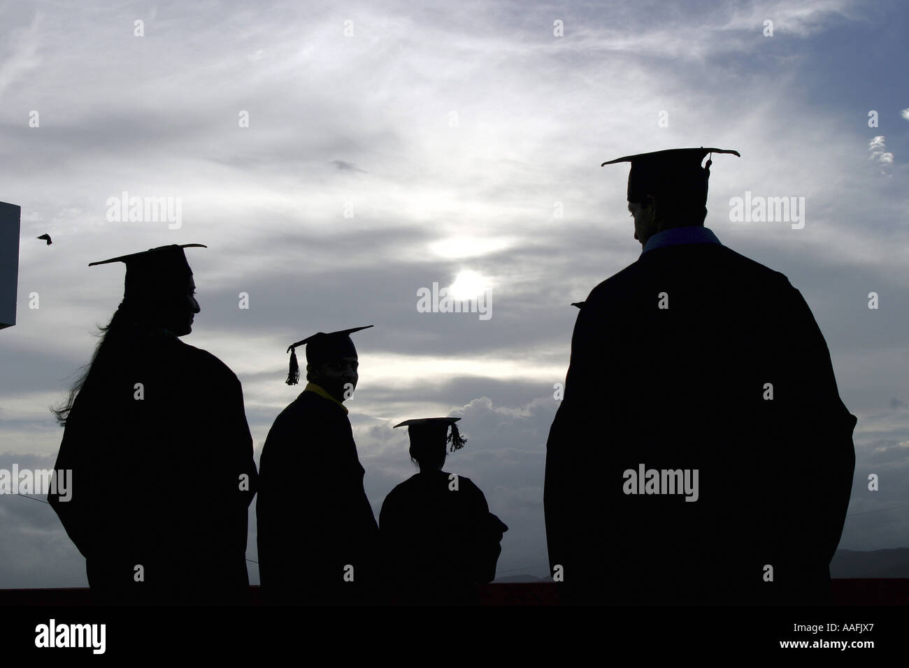 Cuatro jóvenes graduados Tres hombres y una mujer amigas usando vestido de graduación Foto de stock