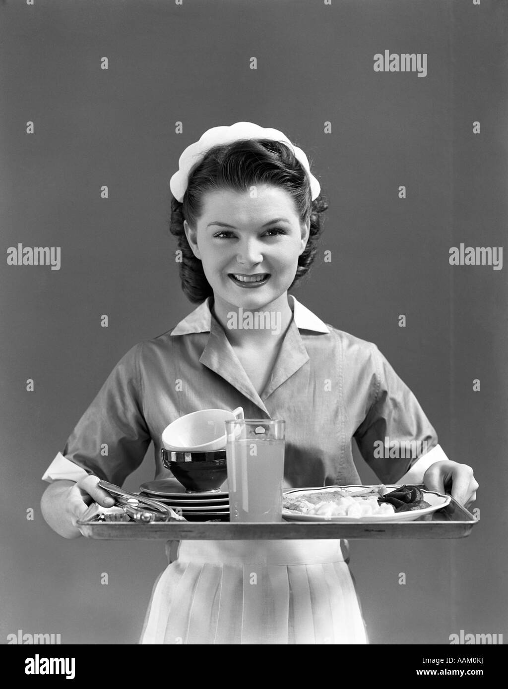 1940 camarera sonriente con un gorro y uniforme con un collar blanco y  delantal sosteniendo una bandeja de servir mirando a la cámara Fotografía  de stock - Alamy